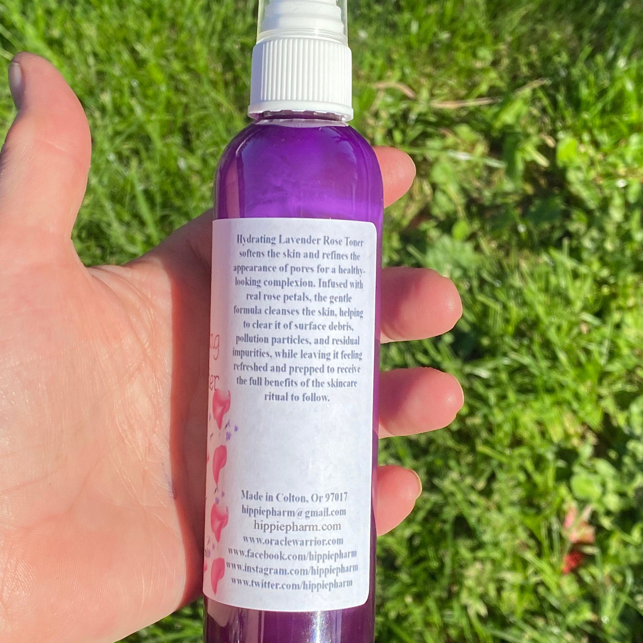 Purple toner bottle with white cap and label, held in hand against green grass background