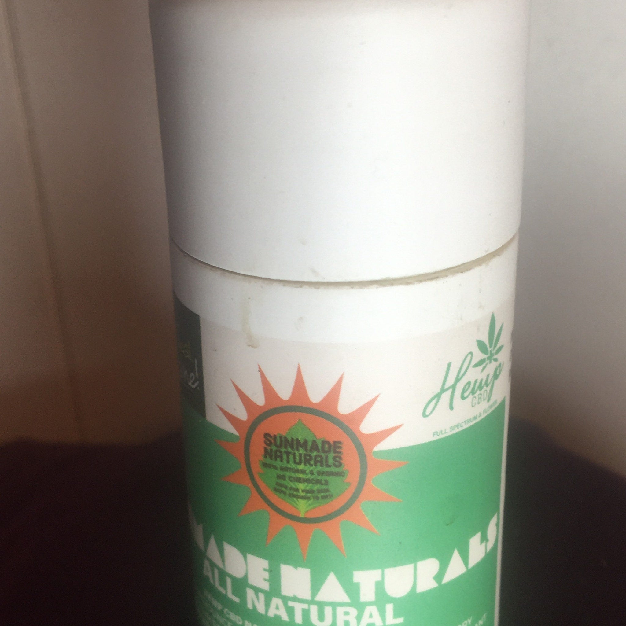 CBD product container, white and green cylindrical packaging, Sunmade Naturals branding visible