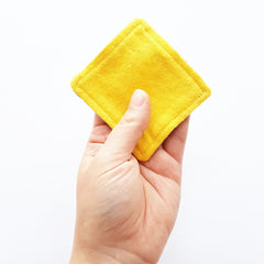 Yellow square fabric pad held in hand, with visible stitching and textured material