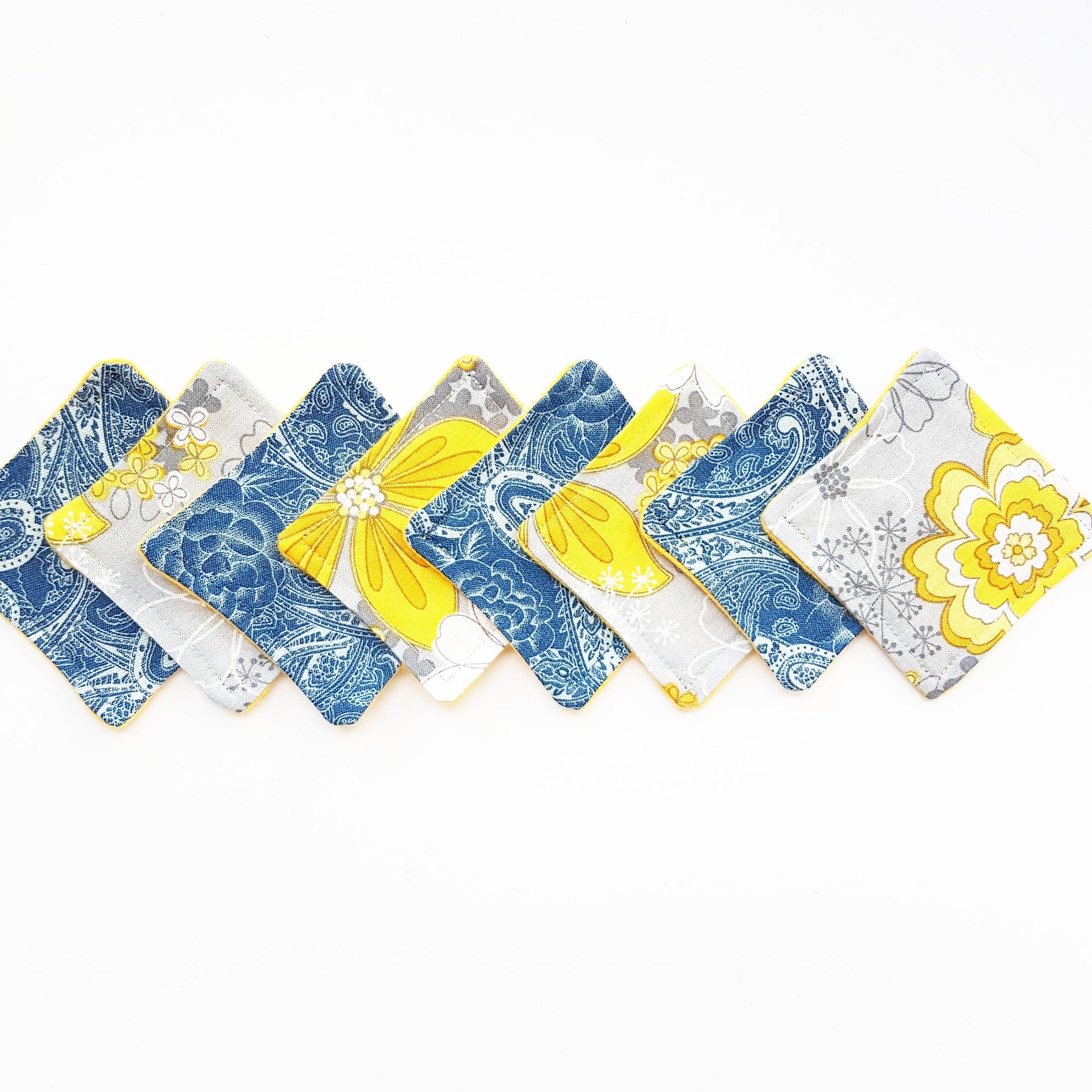 Coasters with floral and paisley patterns in blue, yellow, and gray with yellow trim