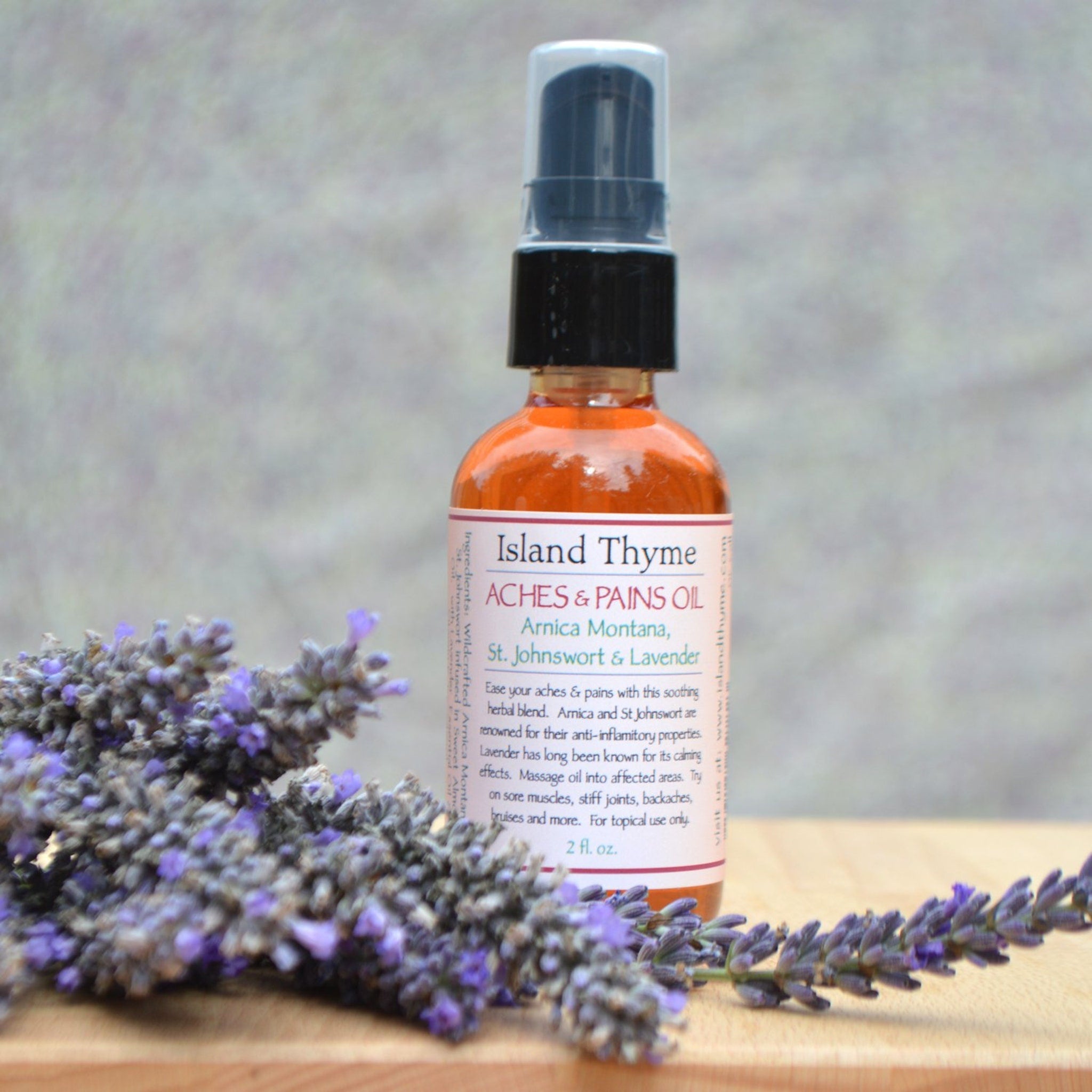 Aches and pains oil bottle with orange liquid, black cap, and lavender flowers on wood surface