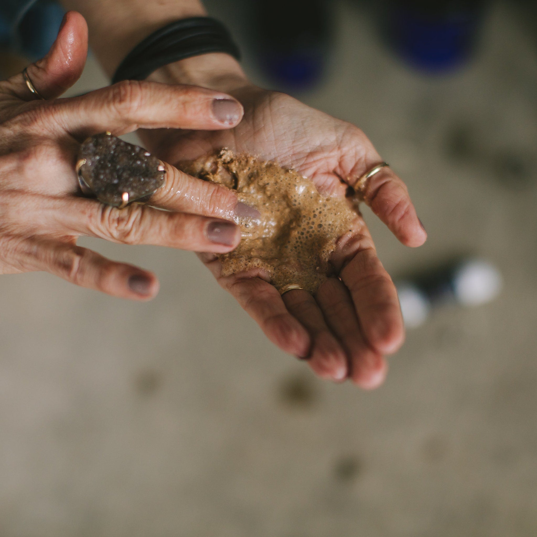 Hands holding brown foamy substance, wearing rings, with light skin tone