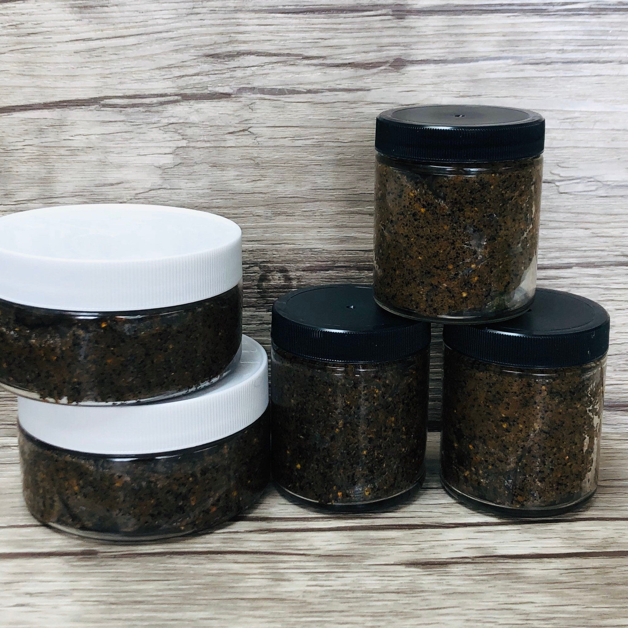 Jarred scrub with black and white lids, clear glass jars, and brown scrub contents.