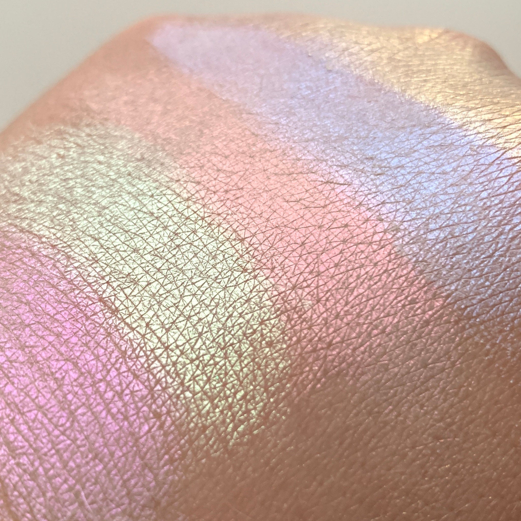 Highlighter swatch with iridescent pink, green, and gold shimmer on skin texture