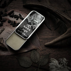 Lip balm tin with black label, silver metal, and Baba Yaga text, on wood surface