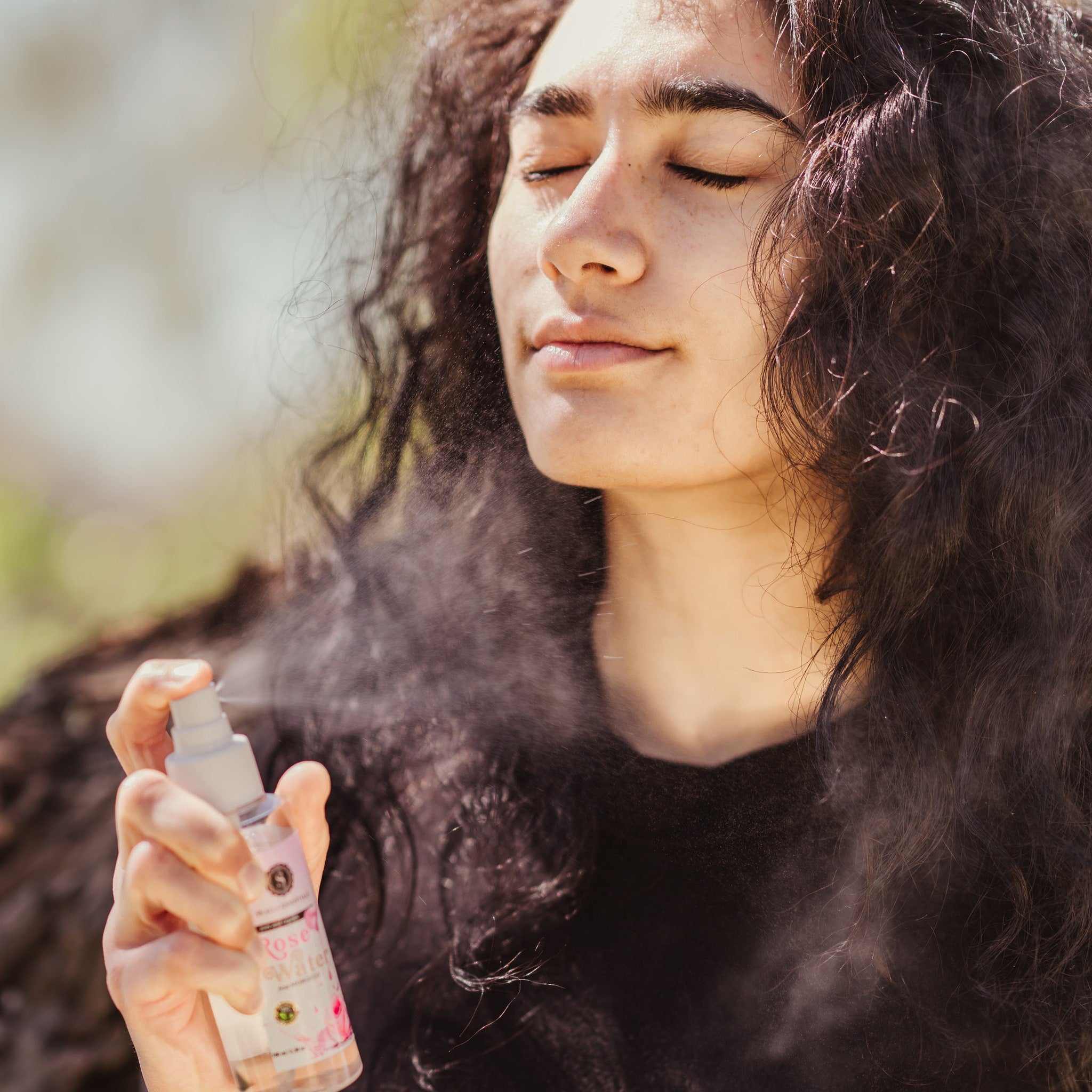Facial mist spray bottle, white plastic, pink label, Rose Water text, being sprayed on face
