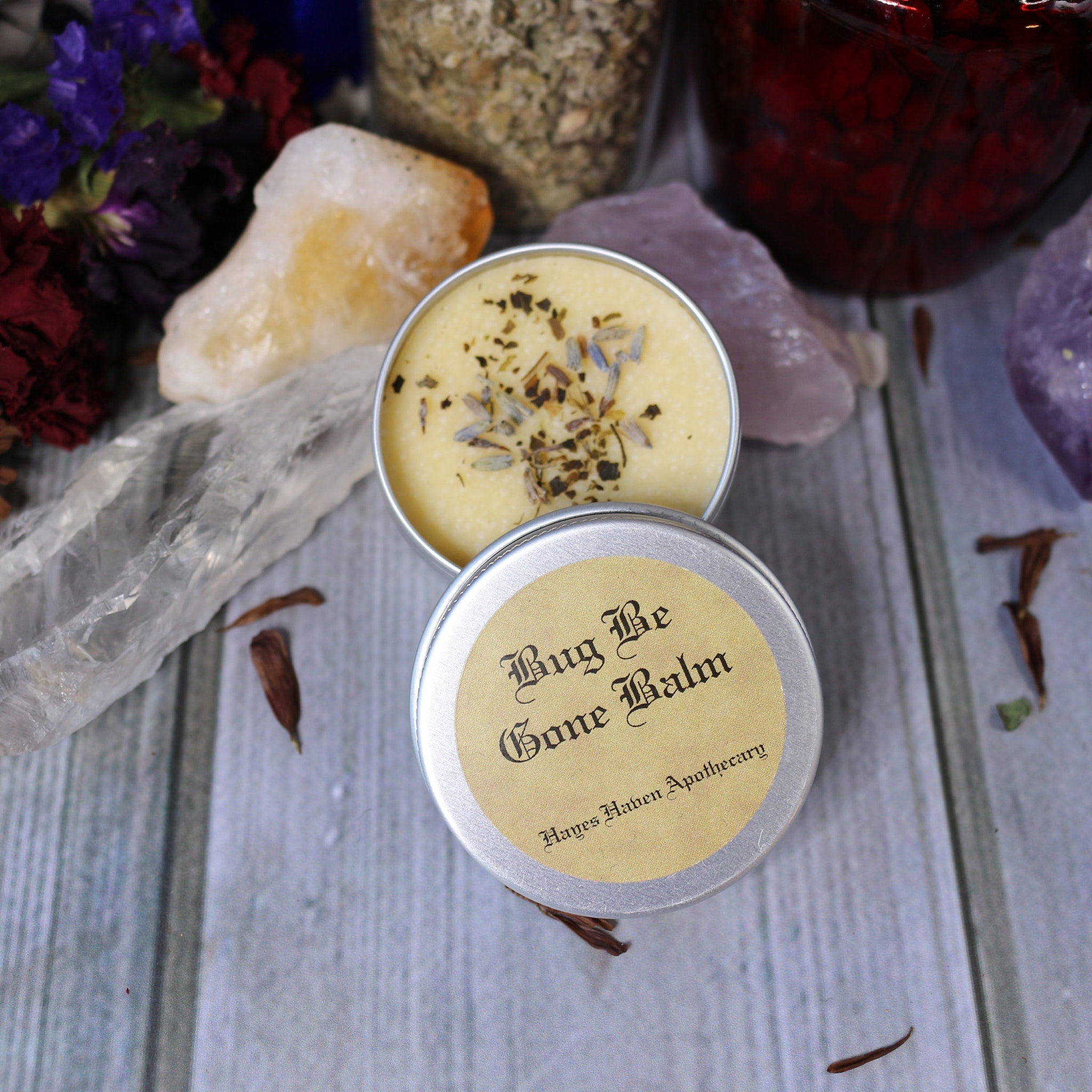 Bug balm in silver tin with yellow label, light yellow balm with herbs, and Hages Haven Apothecary text