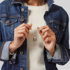 Silver pendant necklace with silver chain, held by hands, worn with denim jacket