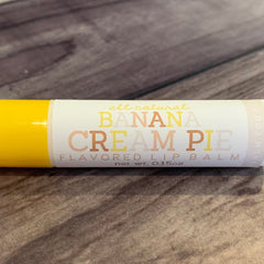 Lip balm tube with yellow and white, banana cream pie text, on wood surface