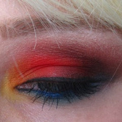 Hand applying matte red eye shadow to eyelid with fingertip for bold makeup look