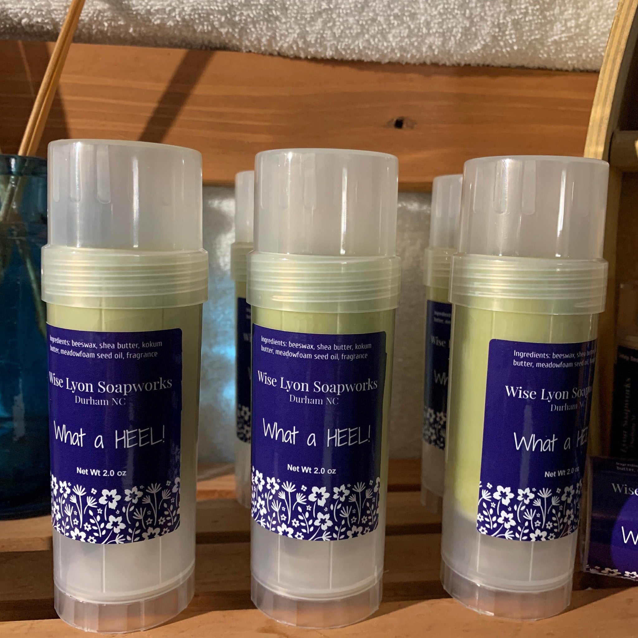 Heel balm sticks with white lids, green balm, and Wise Lyon Soapworks label with floral design