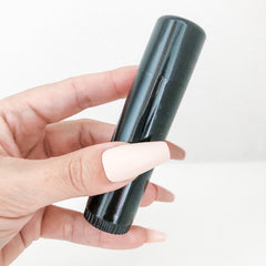 Black tube with shiny finish held in hand with long nude nails