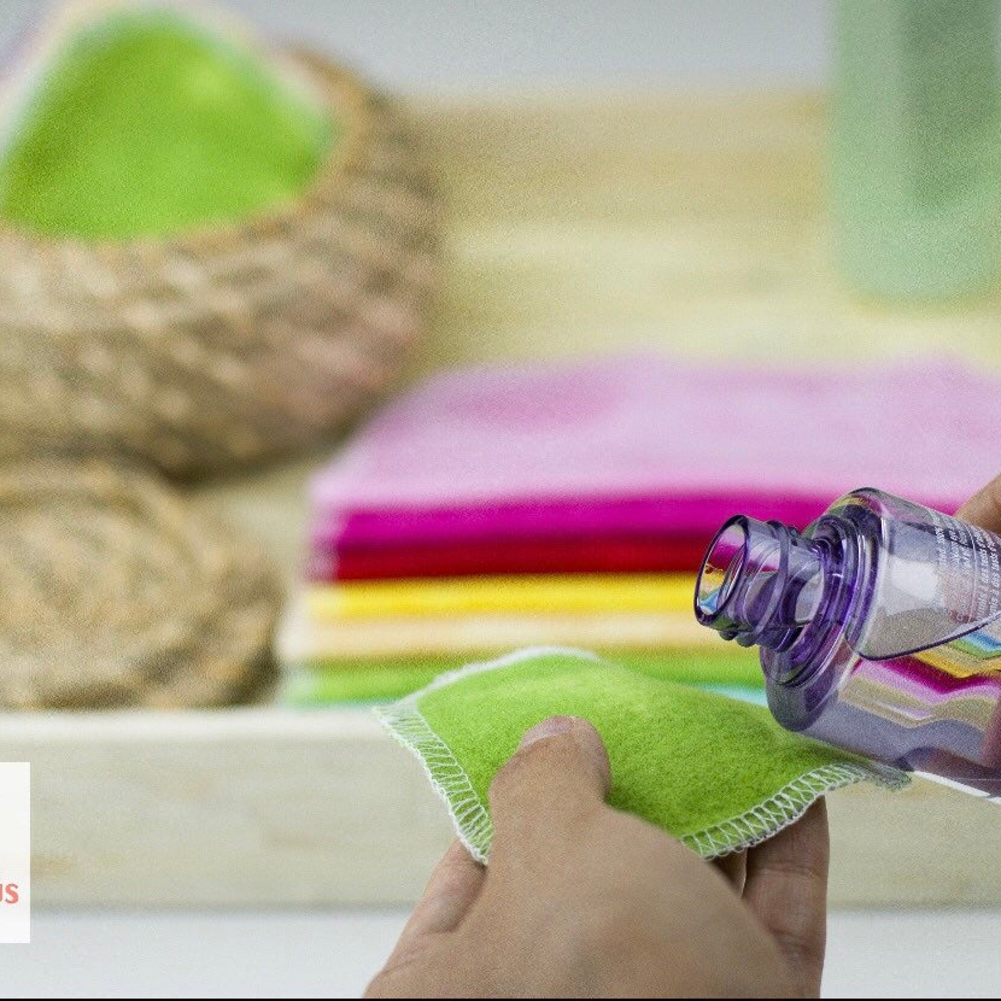 Green cloth pad with white stitched edge, purple bottle dispensing liquid onto pad.