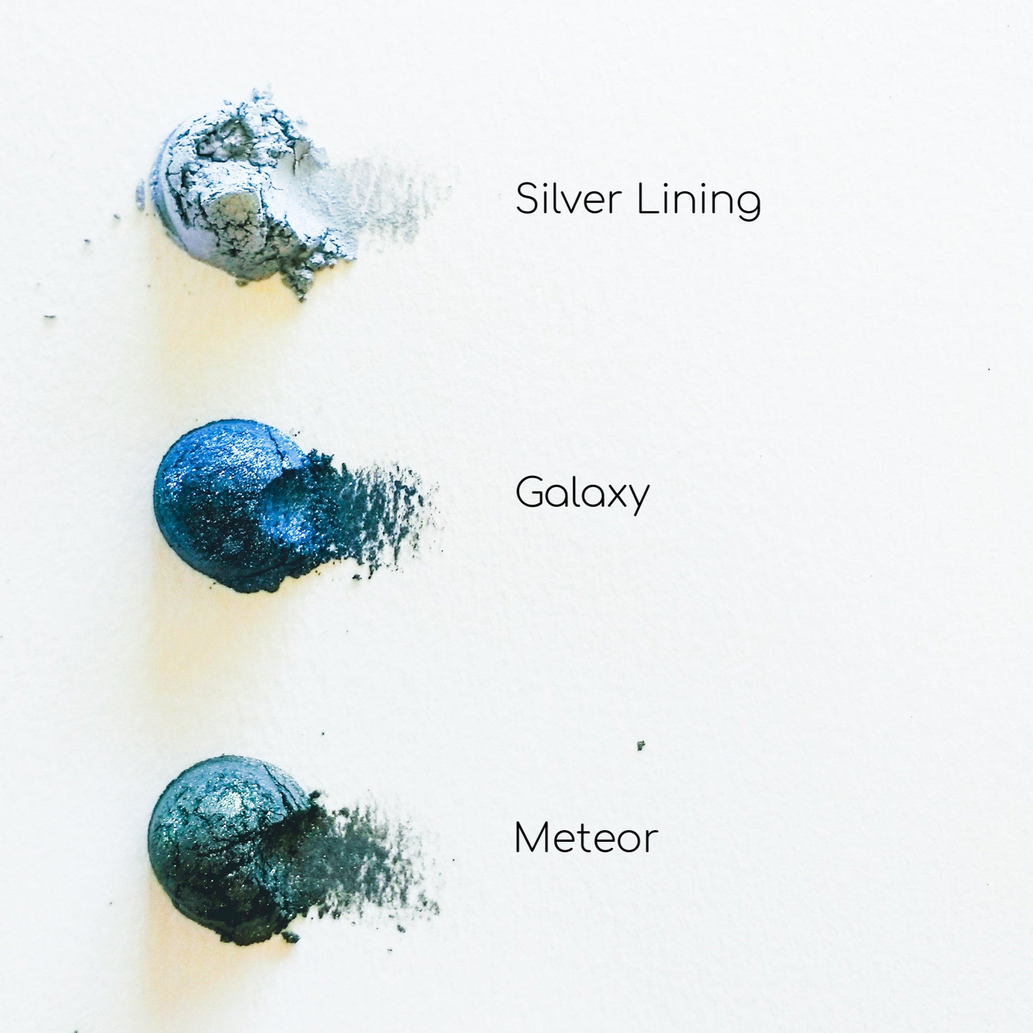 Eyeshadow swatches, various shades of blue and green, metallic finish on white background