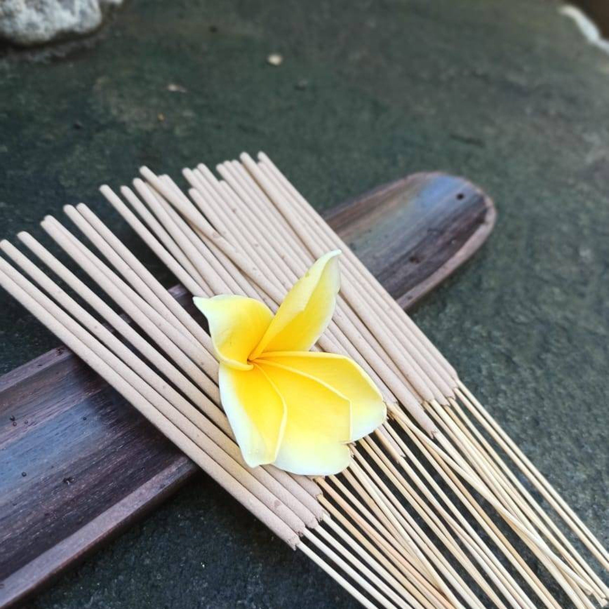 Incense sticks with light brown color, wooden material, and a yellow flower on top of them