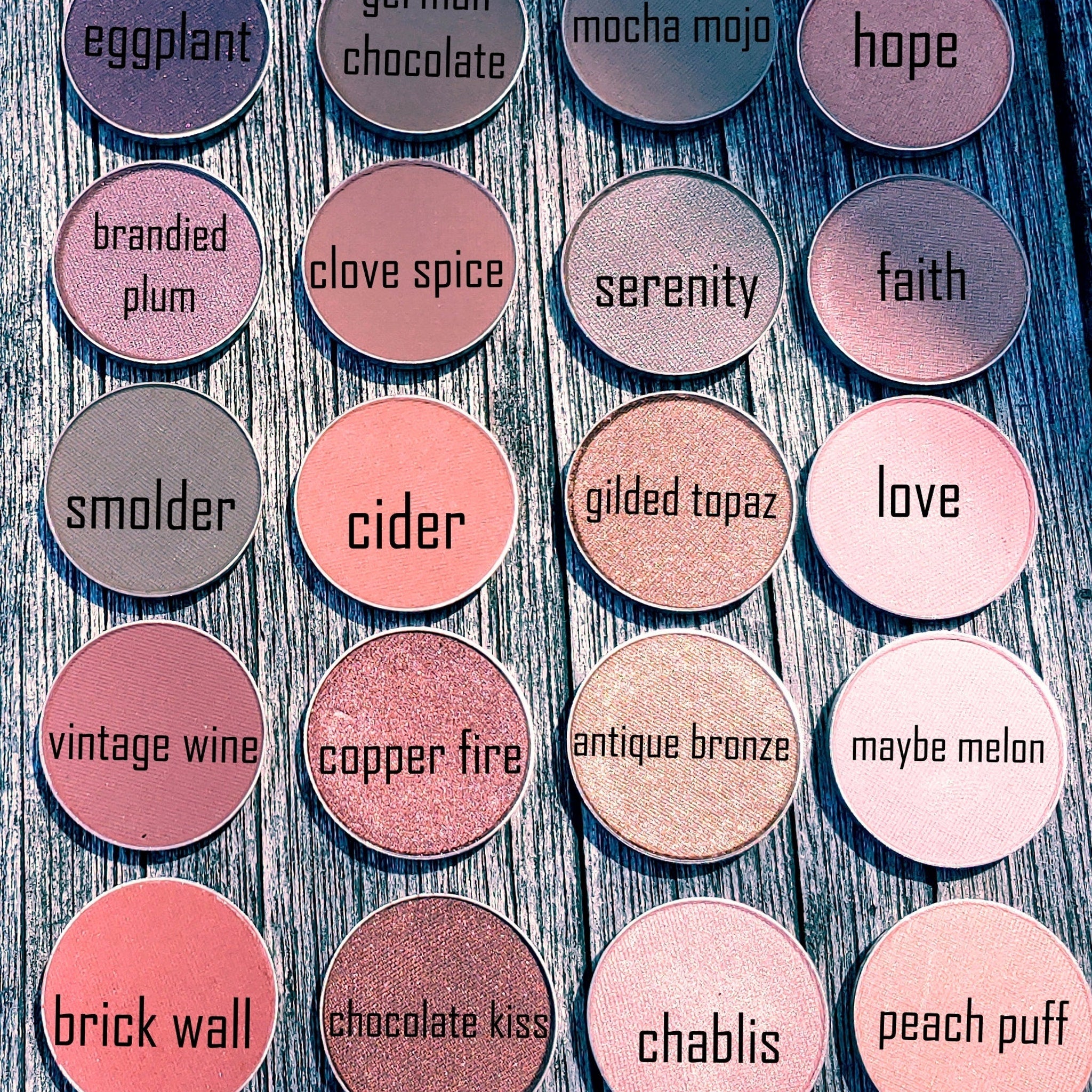 Eyeshadow compacts in various colors with text labels on a wooden surface