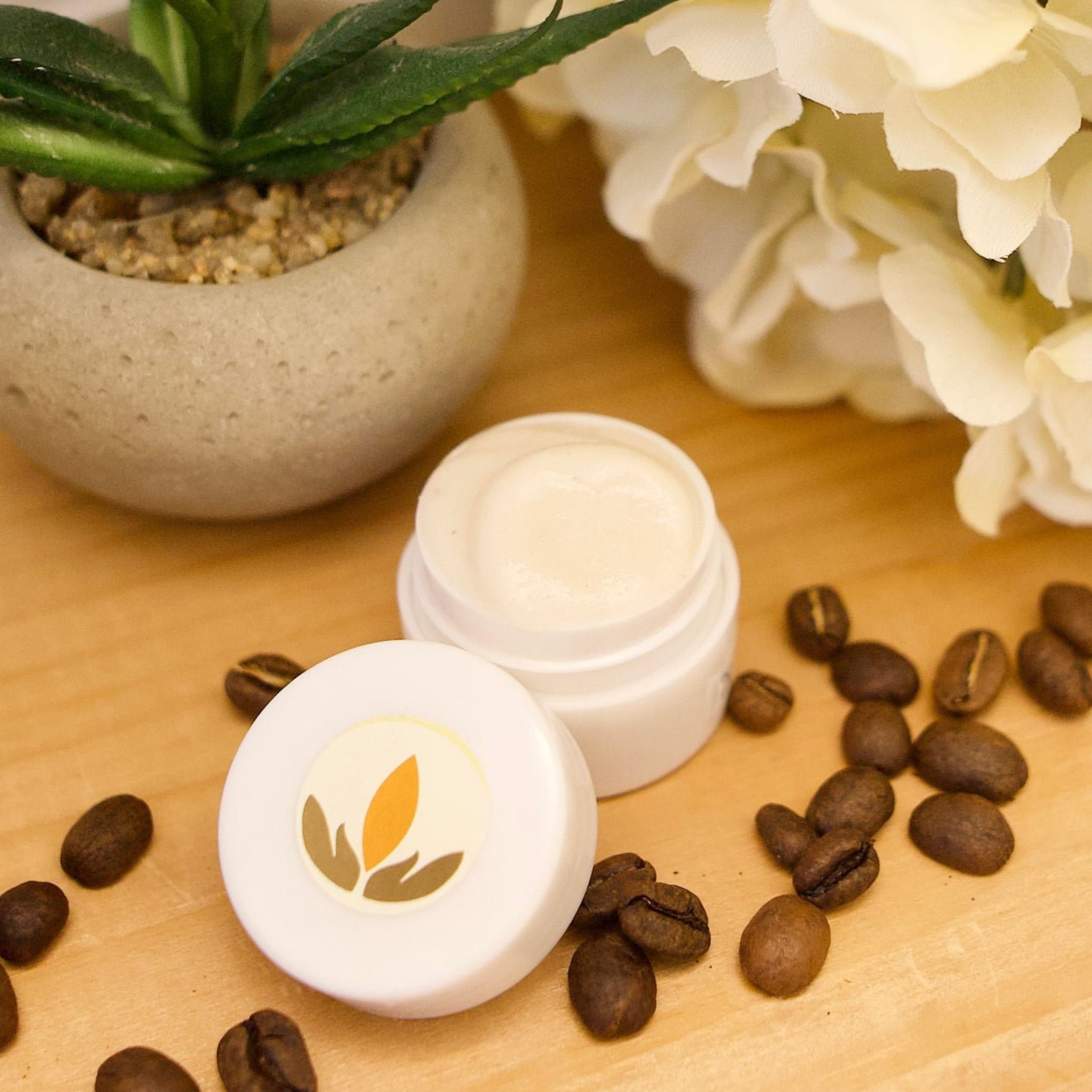 Eye makeup cream in white jar with Mia Botanica logo and coffee beans on wood surface