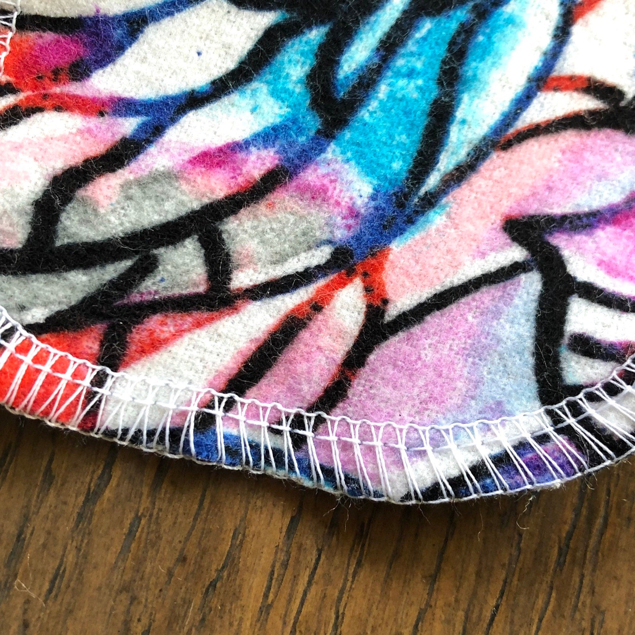 Round fabric with colorful abstract pattern, white stitching, and wood surface background