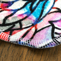 Round fabric with colorful abstract pattern, white stitching, and wood surface background