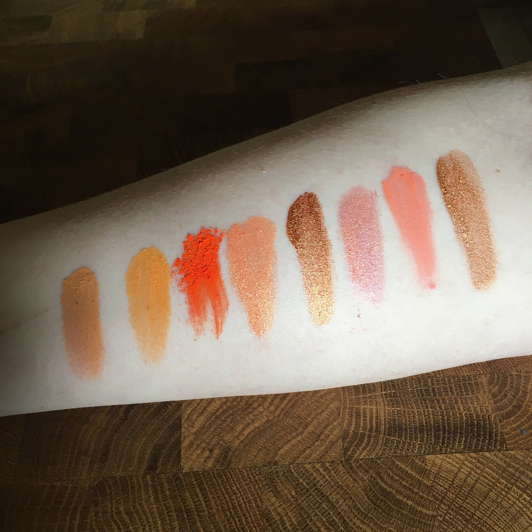Side view of 15 mineral eye shadow samples in round pans showing color gradient from dark plum to shimmering taupe