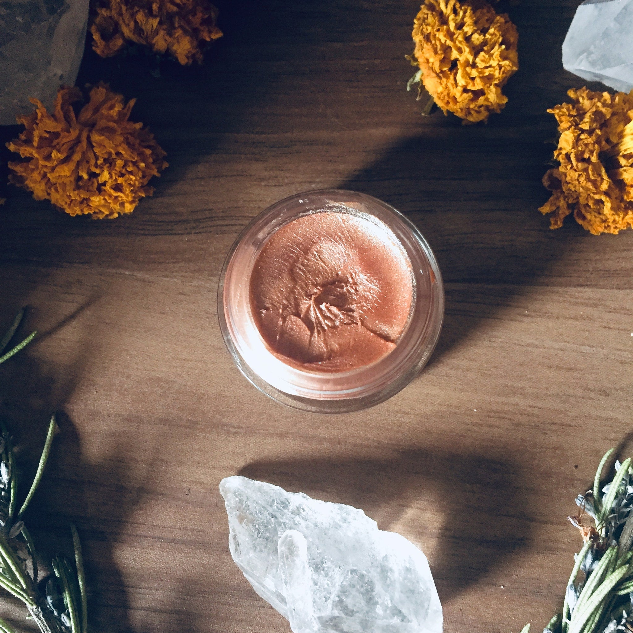 Blush makeup in a glass jar, with peach color and creamy texture, surrounded by flowers and crystals