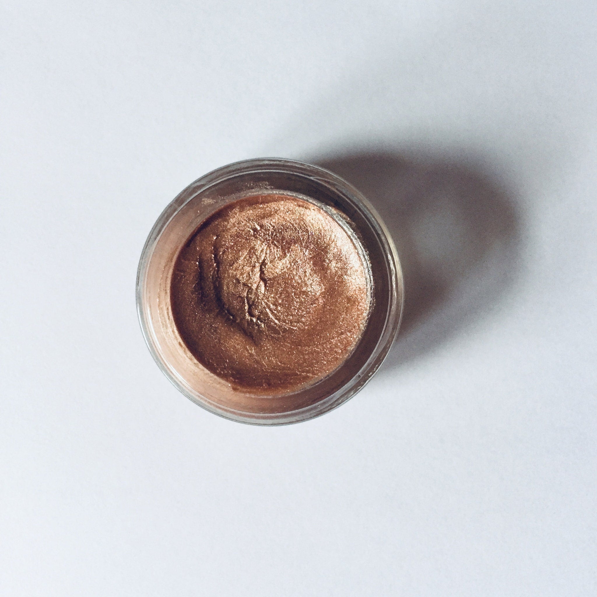Eye shadow pot with bronze metallic color and clear glass container on white background