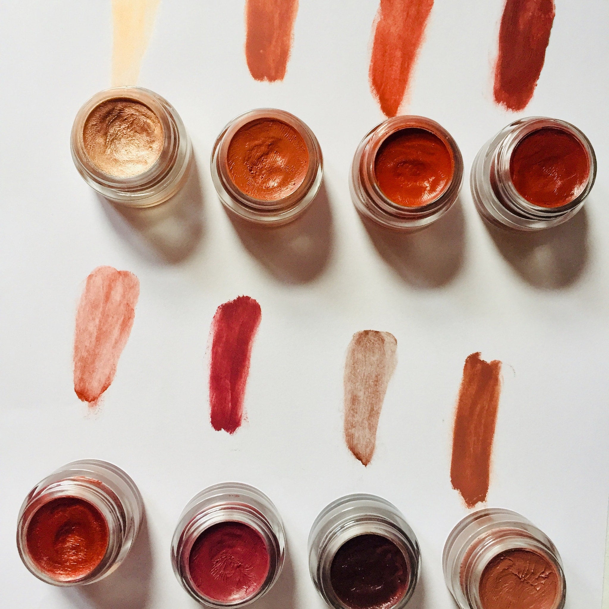 Lip tint swatches in various shades of red, brown, and peach, shown with glass jars and brush strokes