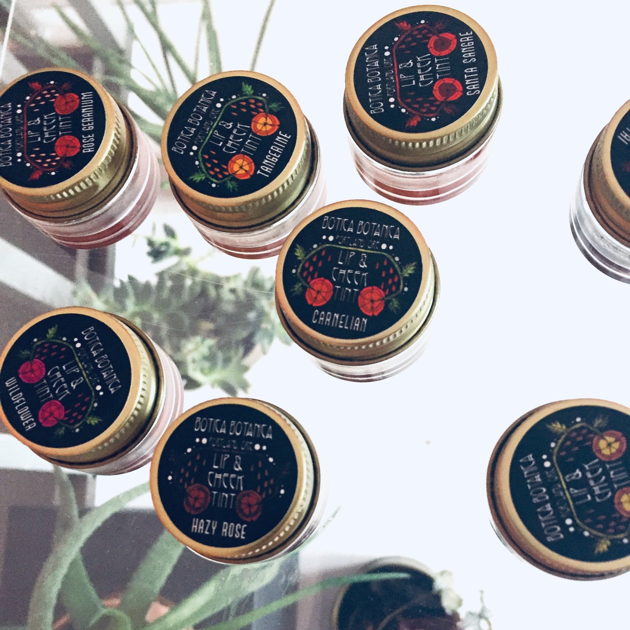 Lip and cheek tint jars with black lids, gold rims, and Botica Botanica branding visible