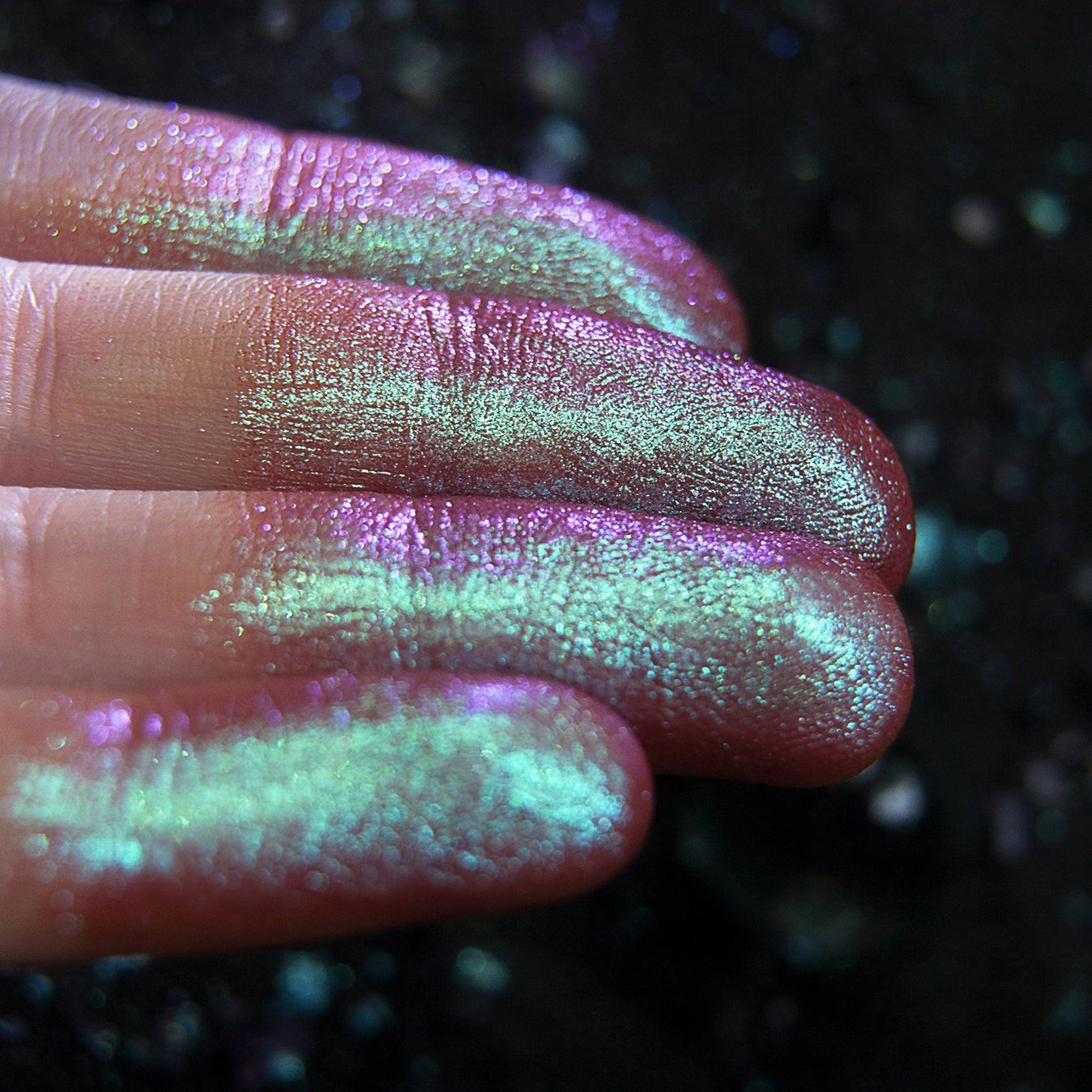 Glitter eyeshadow swatches with pink, green, and iridescent shimmer on fingers