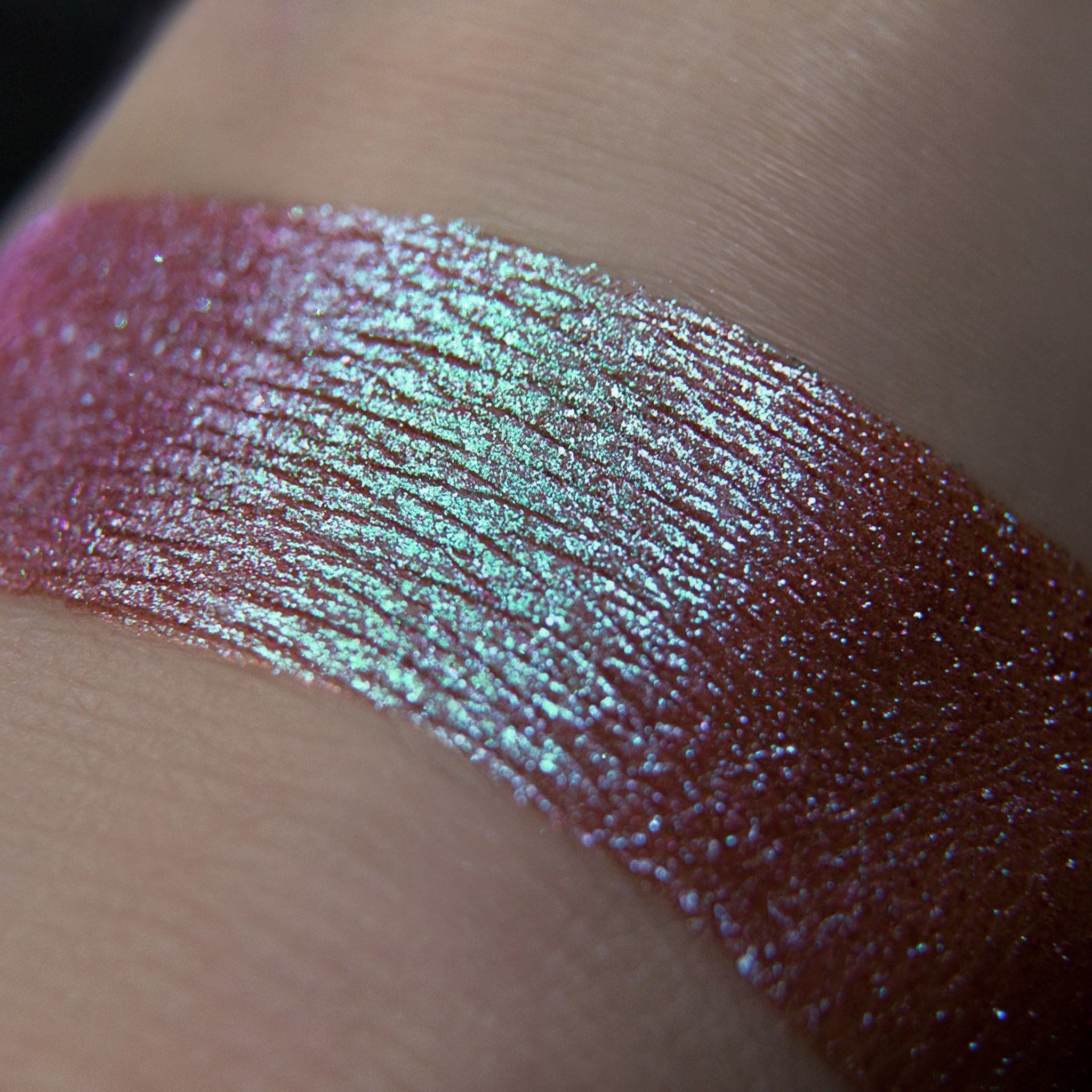Shimmer eyeshadow swatch with iridescent green and pink hues on skin