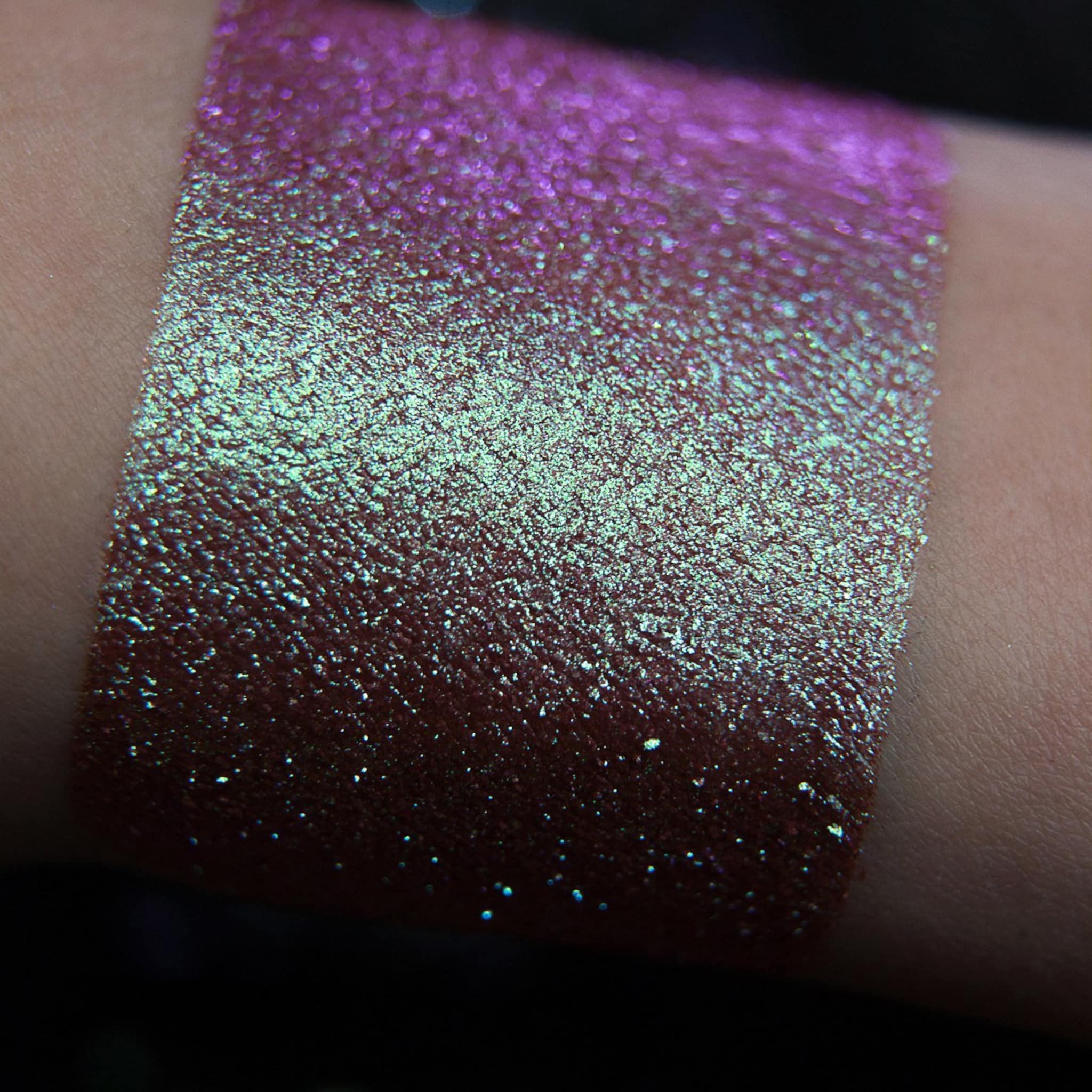 Glitter eyeshadow swatch with purple and teal shimmer on skin, showing color and texture