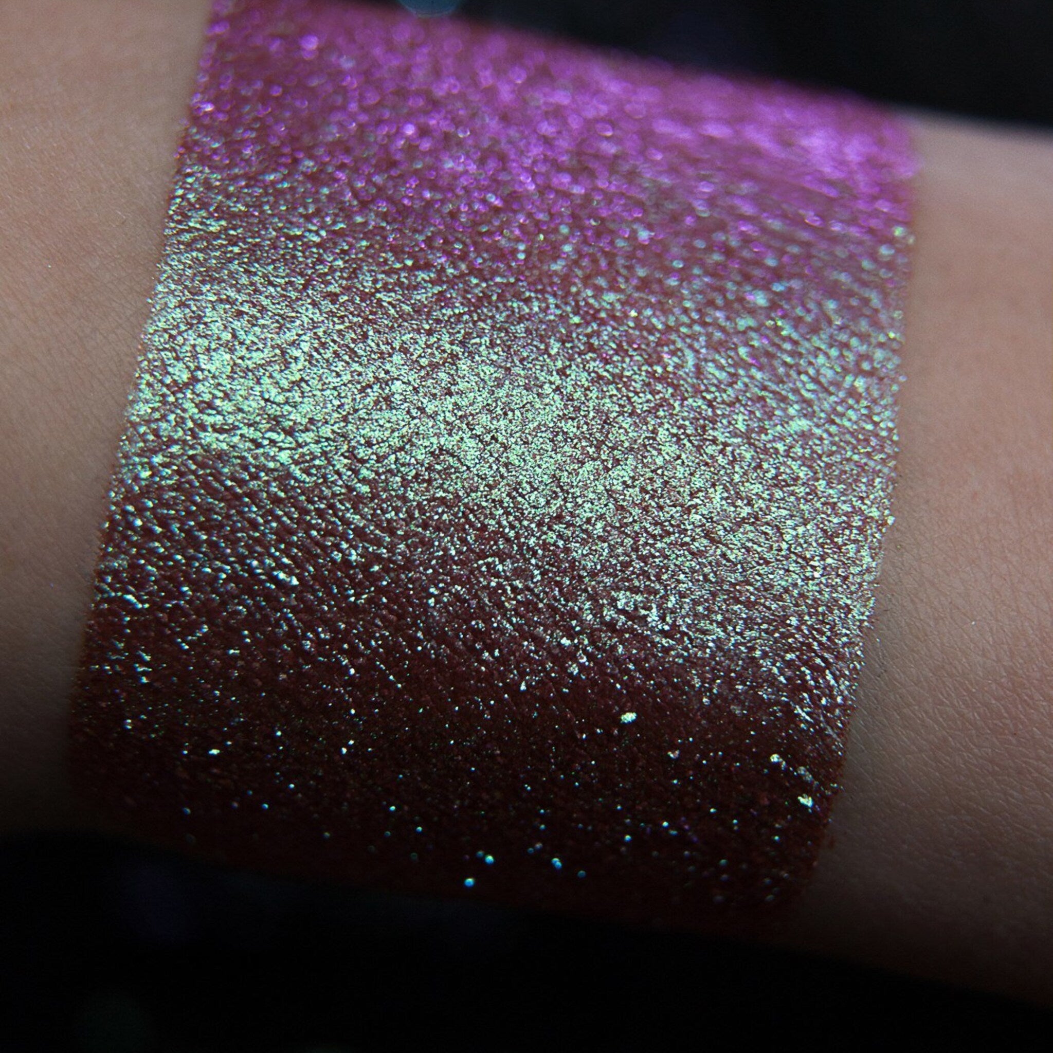 Close-up of fingertips applying shimmery teal and purple mermaid eye shadow to eyelid