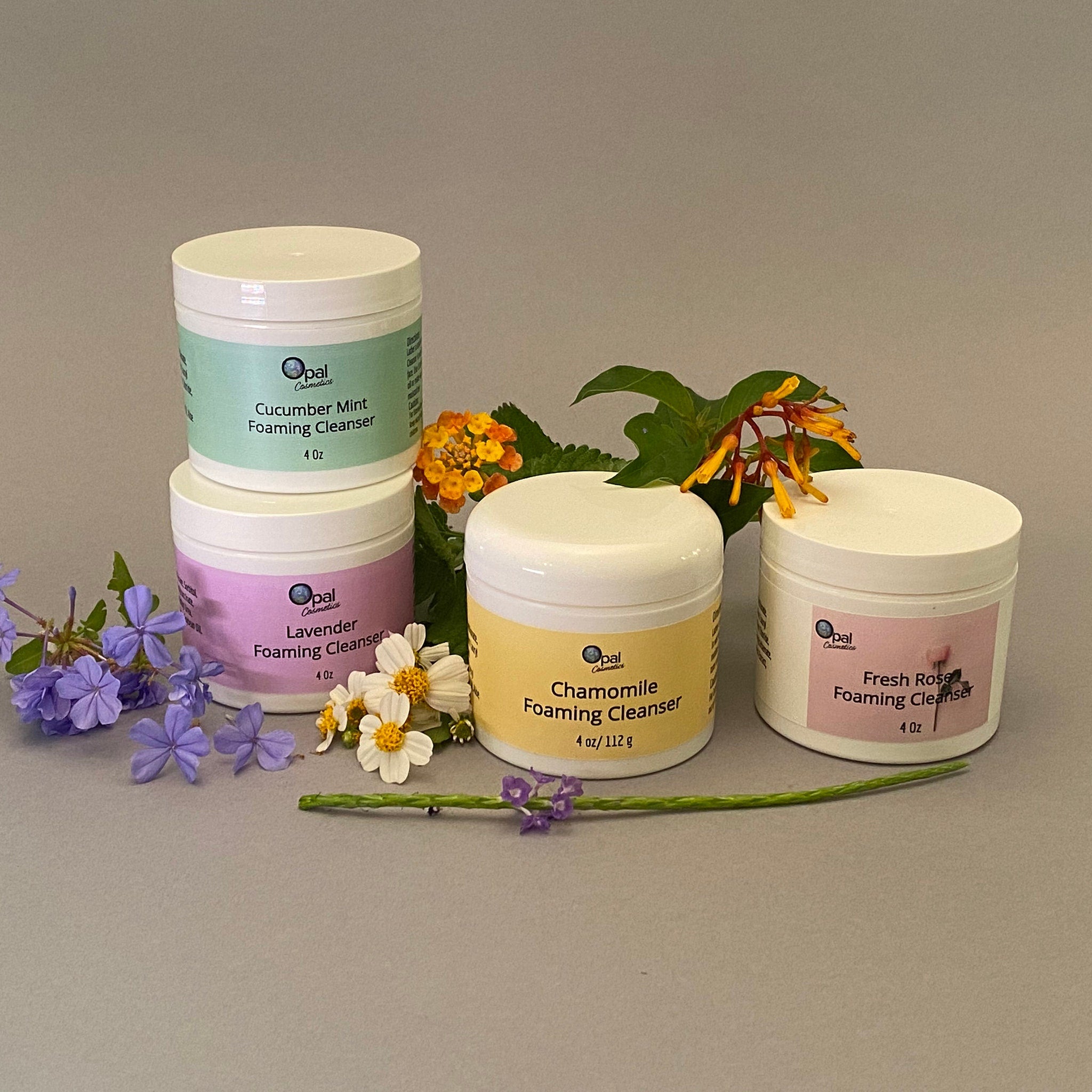 Foaming cleanser jars with white lids, colorful labels, and Opal Cosmetics branding, with flowers
