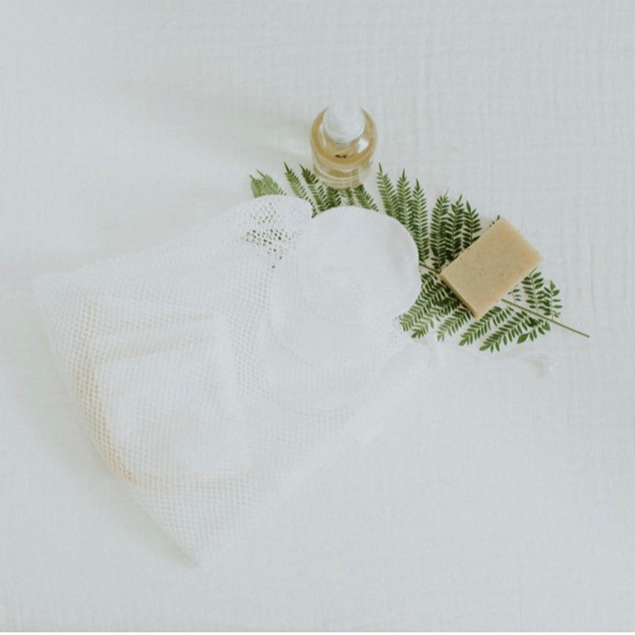 Reusable cotton pads in white mesh bag with soap and greenery on white cloth