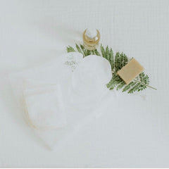Reusable cotton pads in white mesh bag with soap and greenery on white cloth
