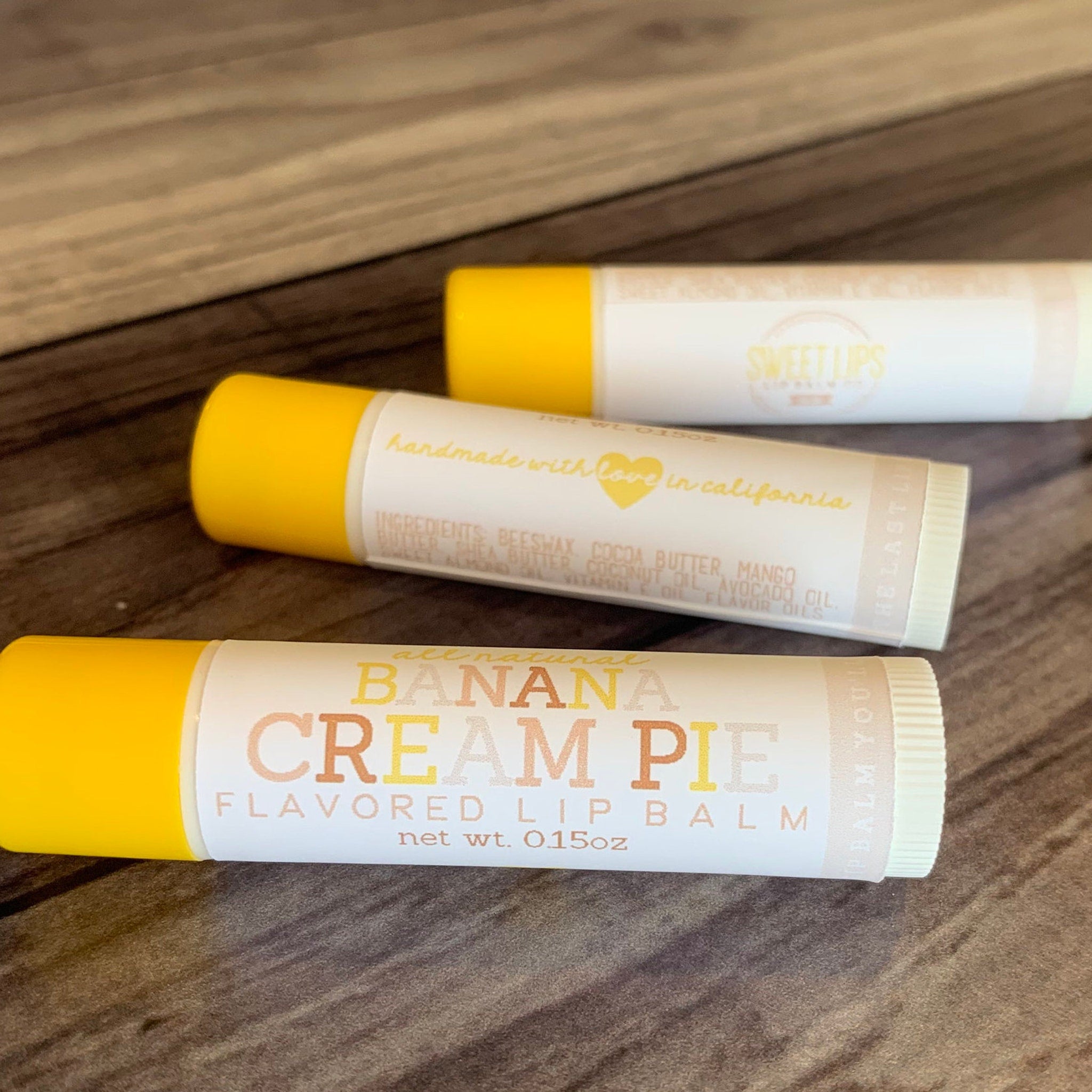 Lip balm tubes with yellow, white, and tan labels, "Banana Cream Pie" text, and "Sweet Lips" visible