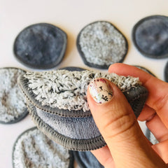 Reusable makeup remover pads, gray plush material with stitched edges, held in hand