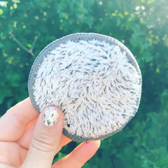 Reusable makeup remover pad with white fluffy material and gray trim, held by a hand