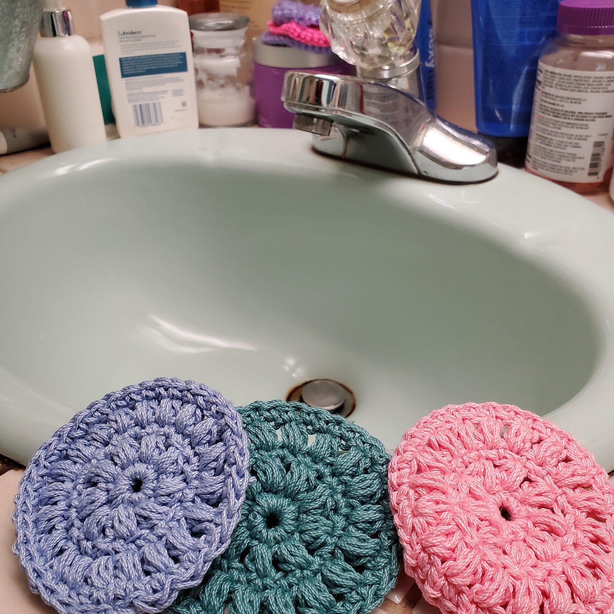 Crochet washcloths in blue, green, and pink, sitting in a bathroom sink