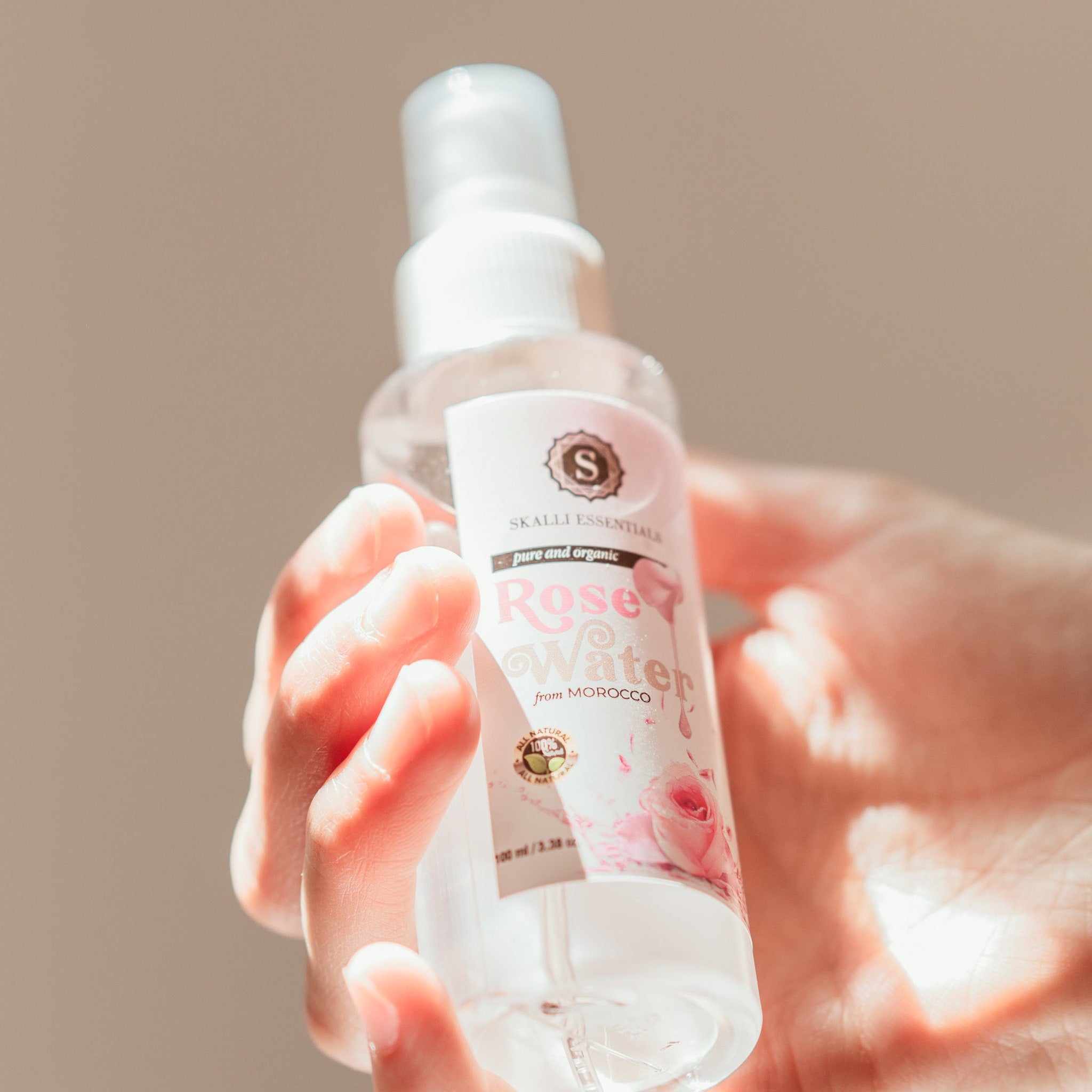 Rose water spray bottle, clear plastic, white cap, held in hand, Skalli Essentials label