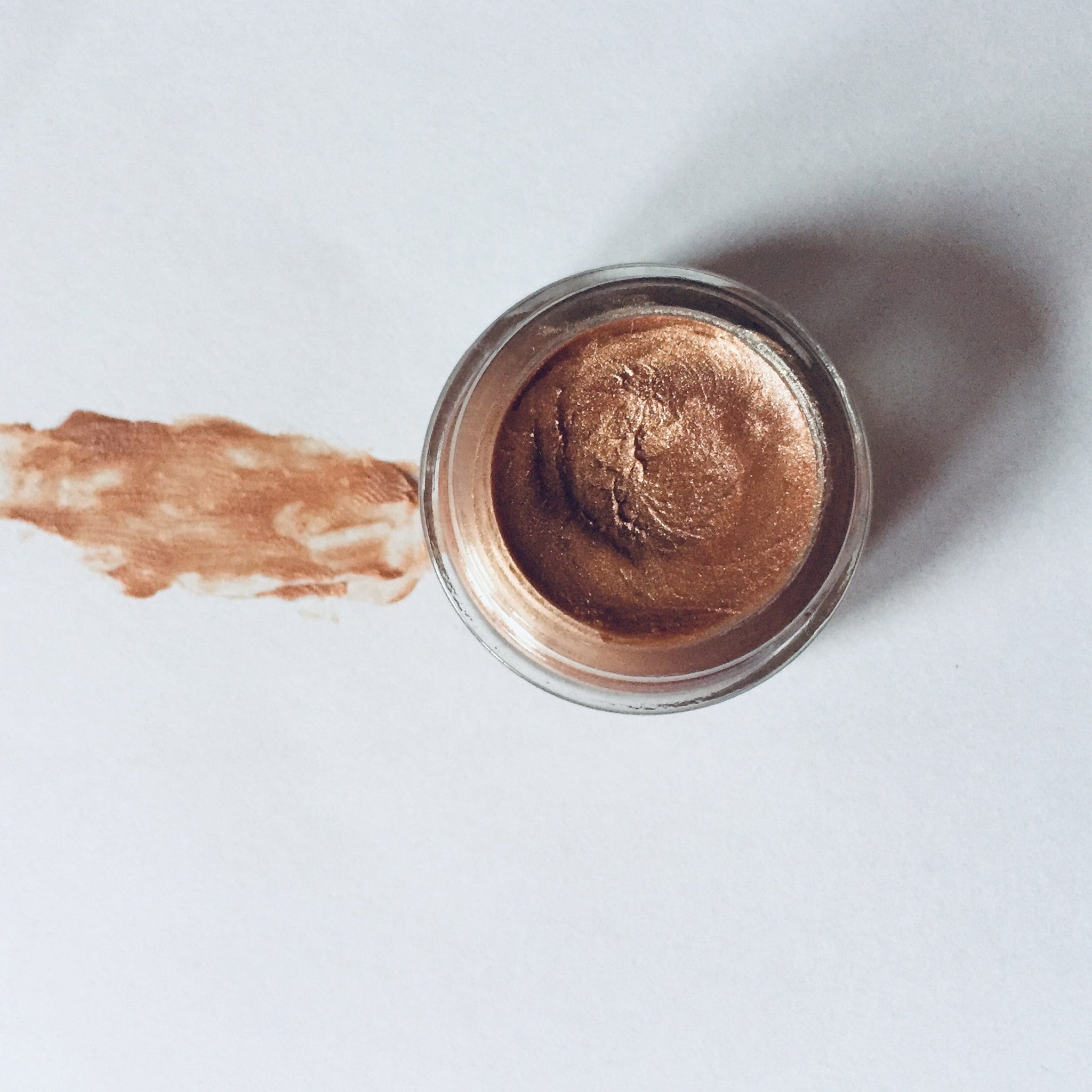 Eyeshadow pot with bronze metallic color and clear glass jar on white background
