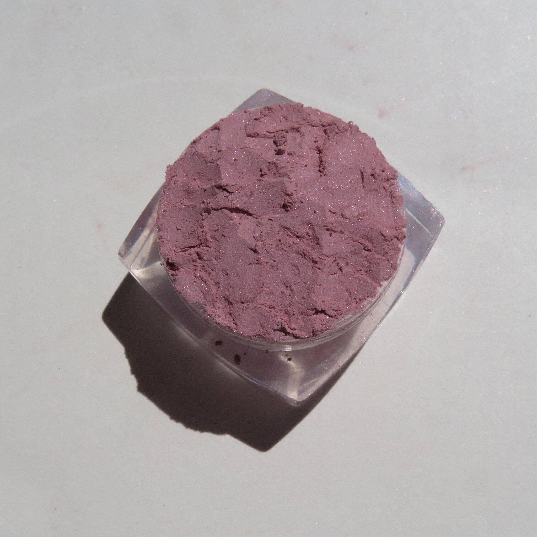 Close-up of loose pale mauve mineral eyeshadow powder with soft shimmer in a compact jar