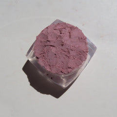 Close-up of loose pale mauve mineral eyeshadow powder with soft shimmer in a compact jar