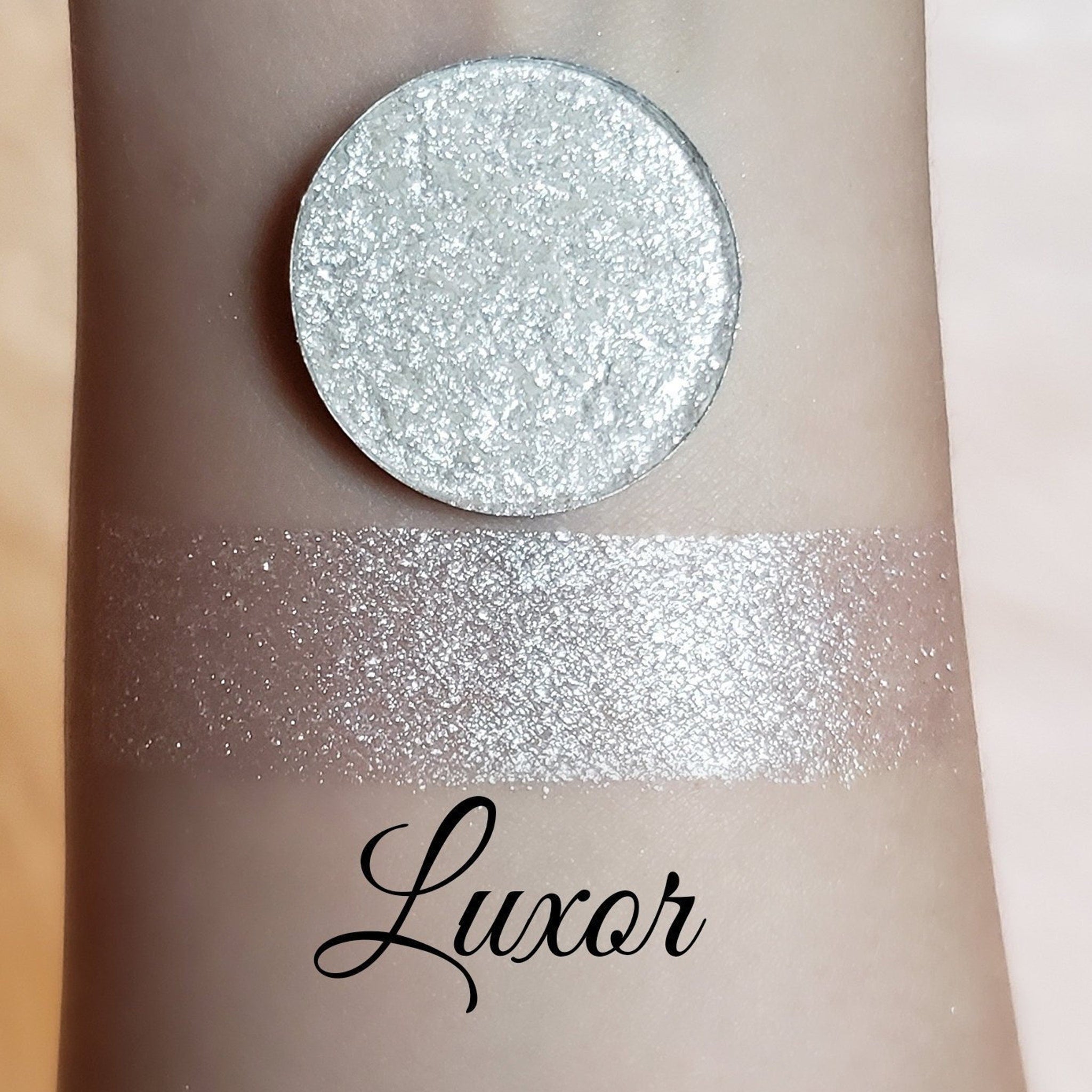 Eyeshadow shimmer pigment, silver pressed powder and swatch on skin, Luxor brand visible