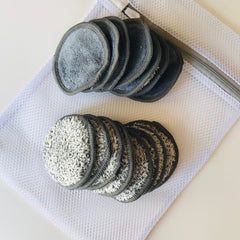 Reusable makeup remover pads in gray and white with a mesh laundry bag on white surface