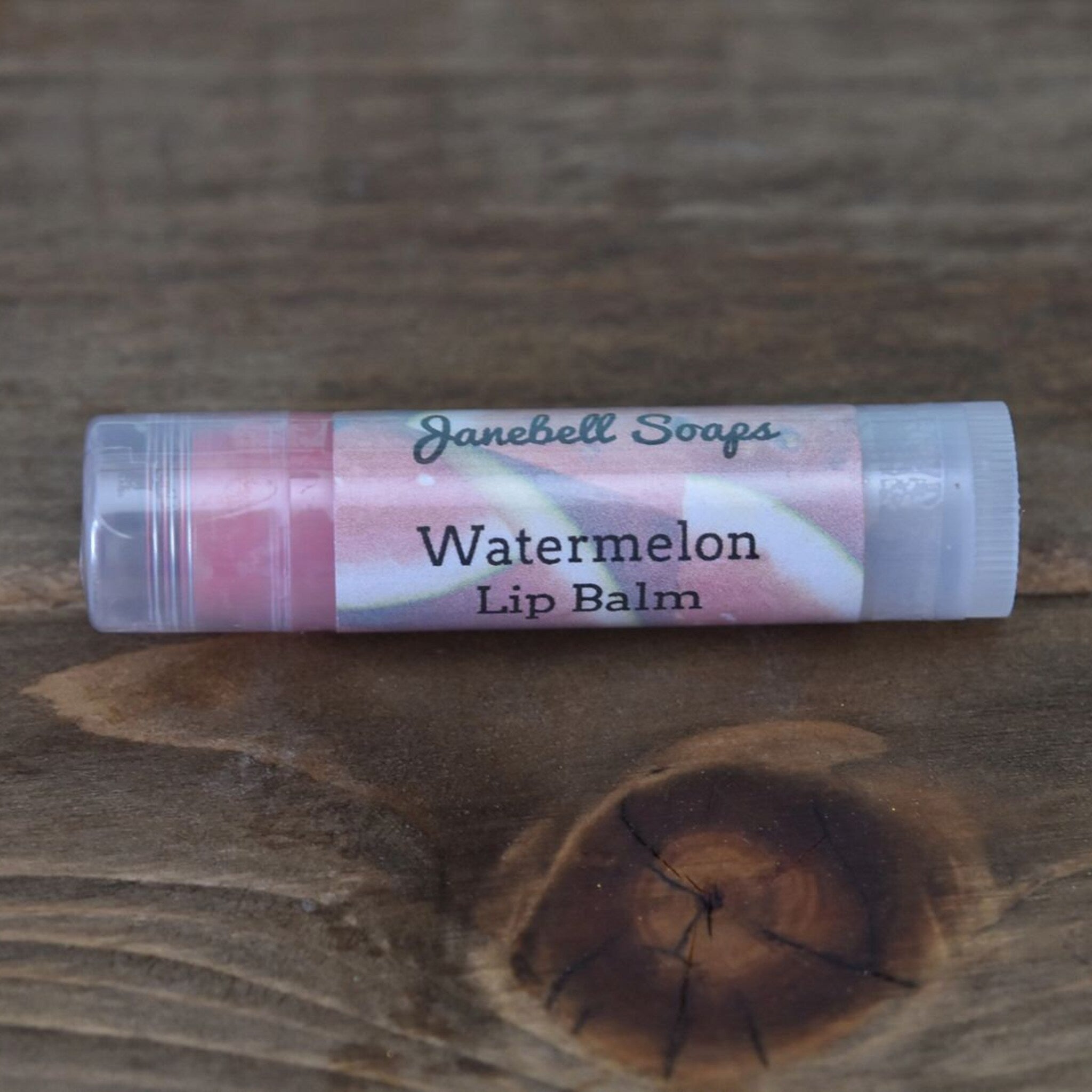 Lip balm tube with pink and white label, clear plastic container, Janebell Soaps brand name visible