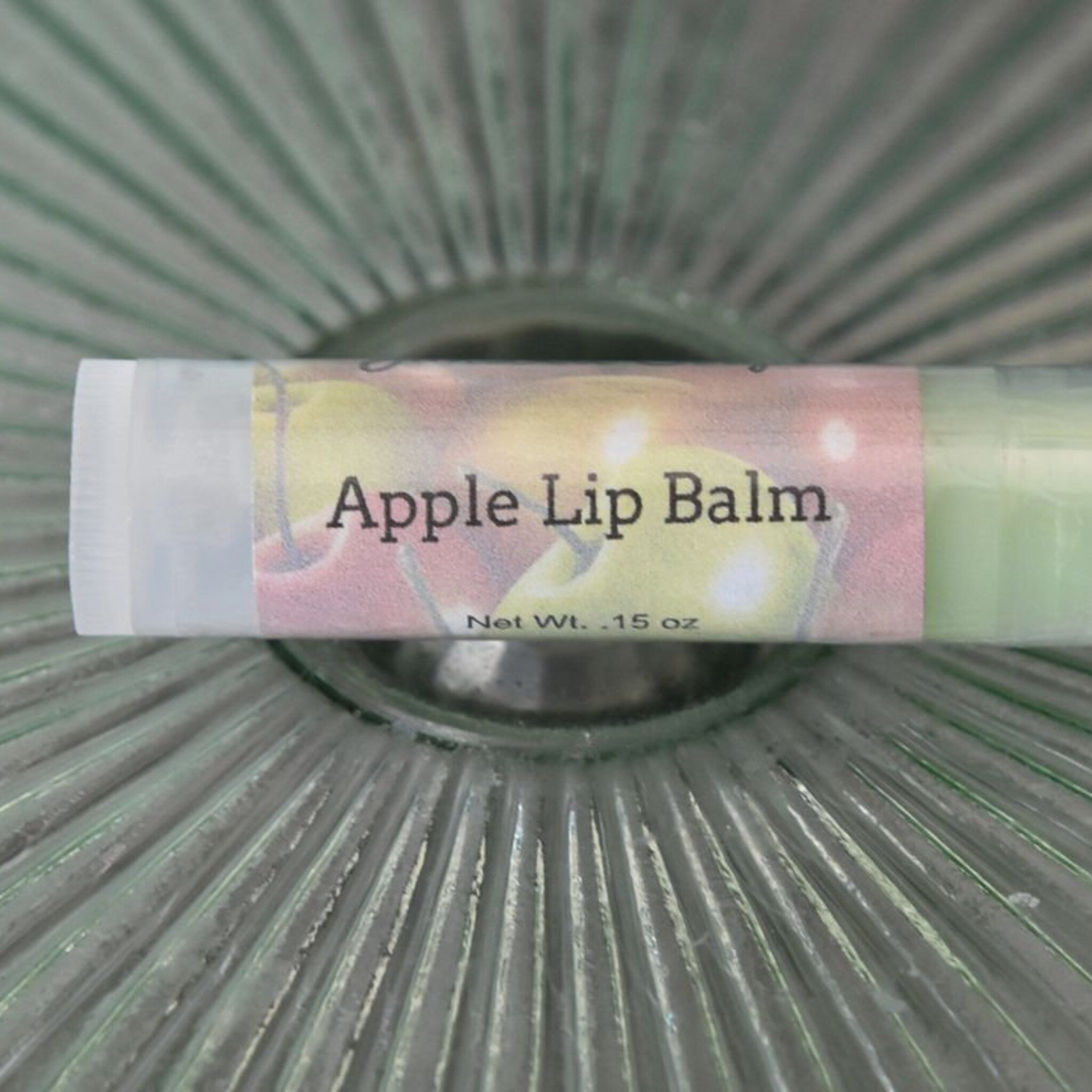 Apple lip balm tube with white, pink, and green label, in glass bowl
