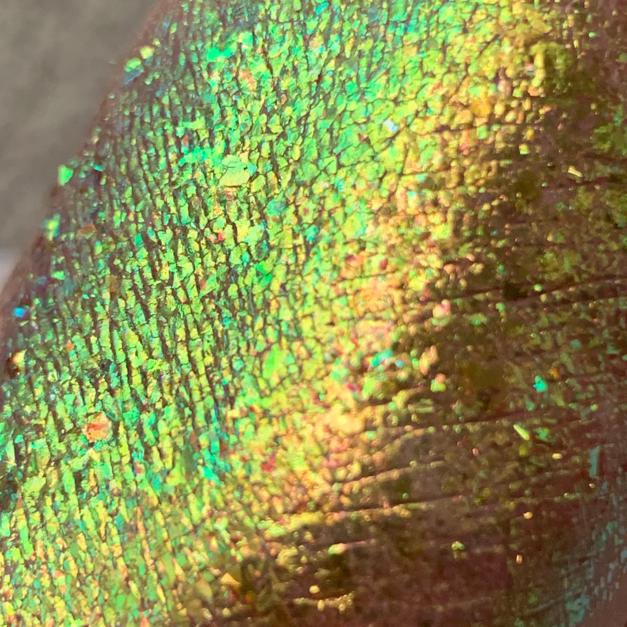 Iridescent green and gold textured surface with cracked pattern and light reflections