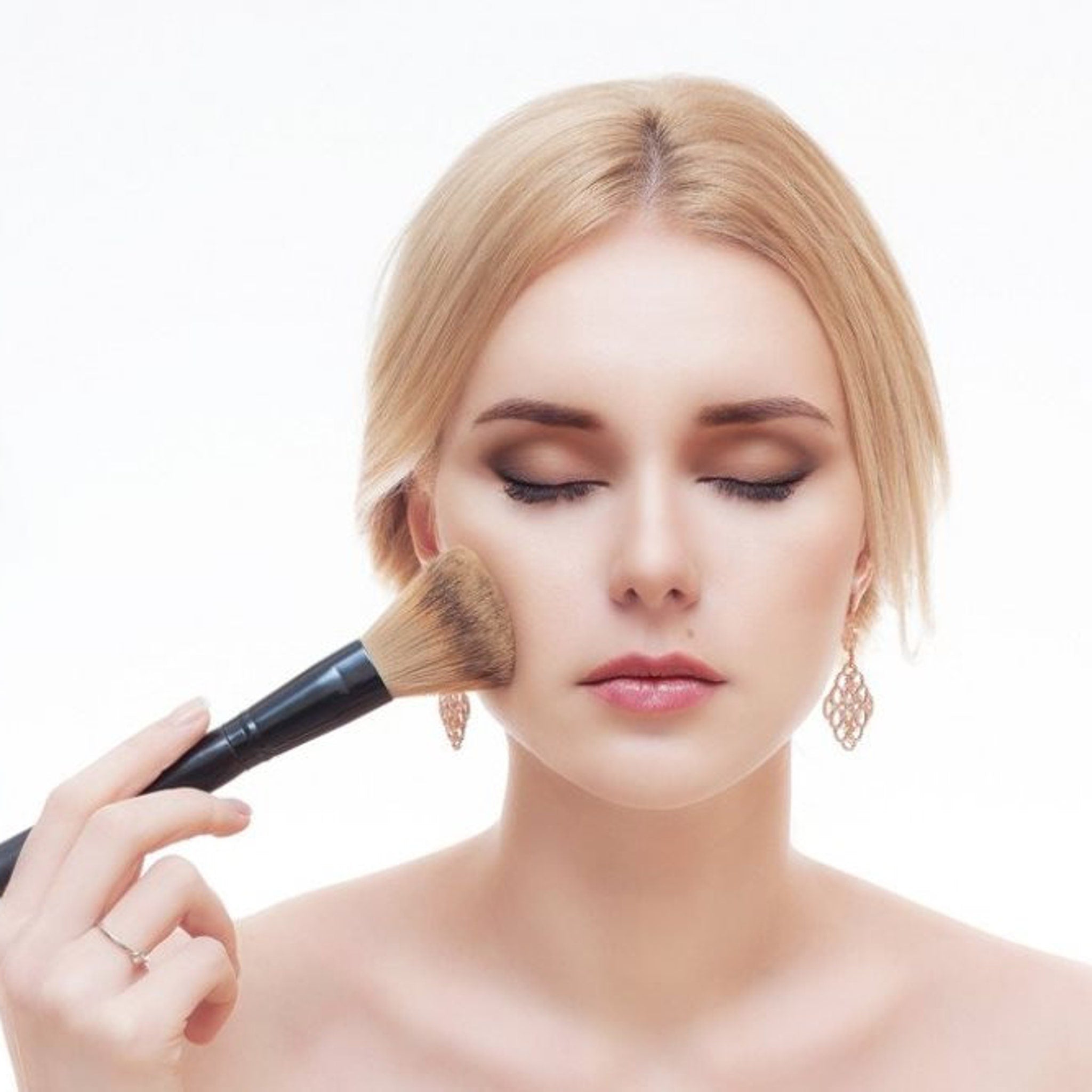 Makeup brush applying powder on fair skin, blonde hair, black handle
