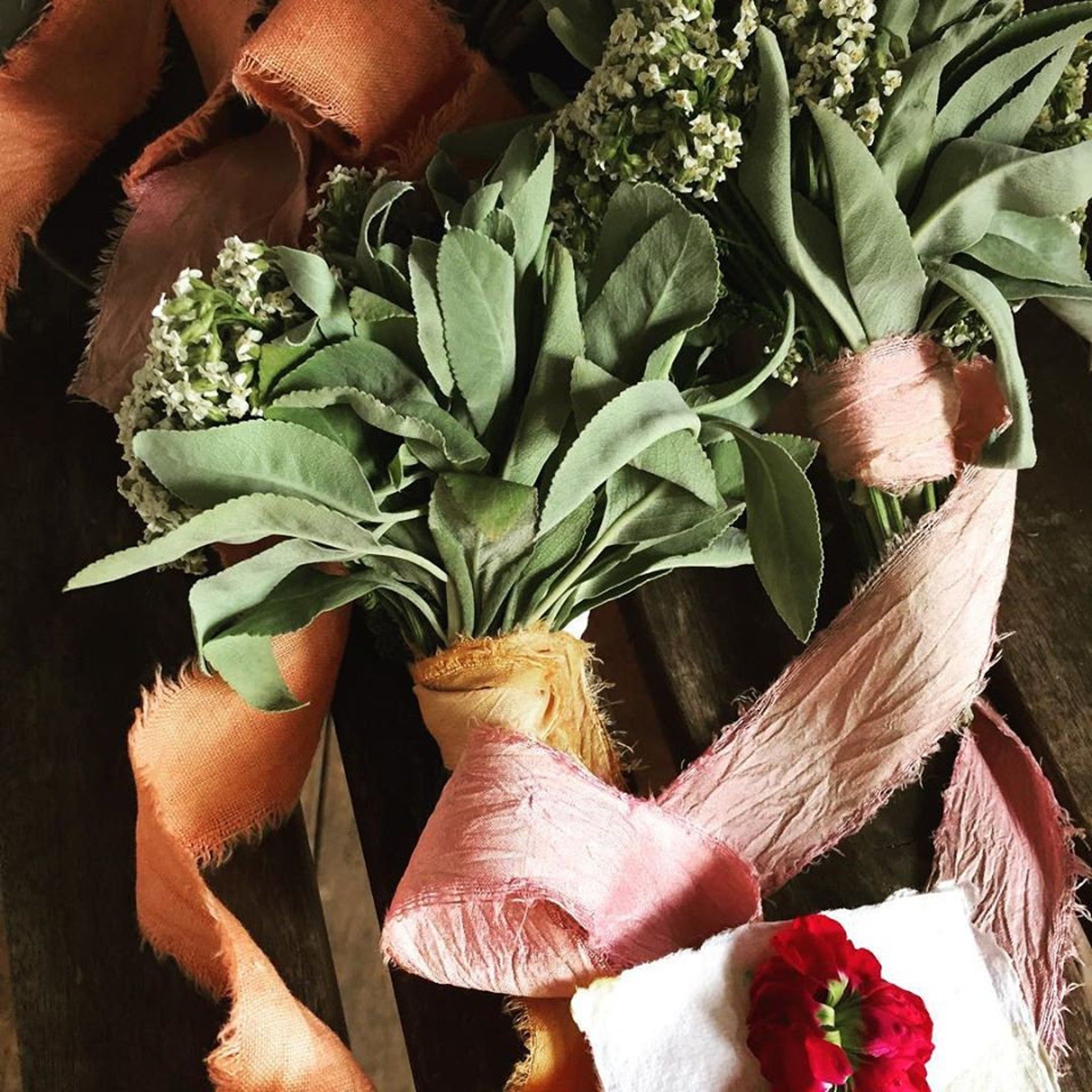 Sage bouquets with green leaves, pink ribbon, and orange burlap trim on wooden surface